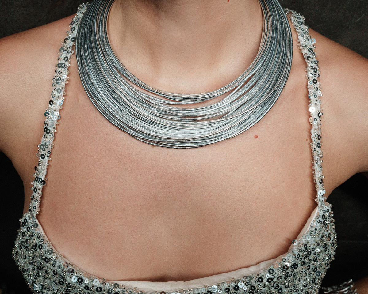 Imperial Strands, A striking silver multi-layered necklace crafted from a blend of bronze, lurex, metal and thermoplastic, offering a modern twist on classic elegance.
Available in gold and silver finishes.